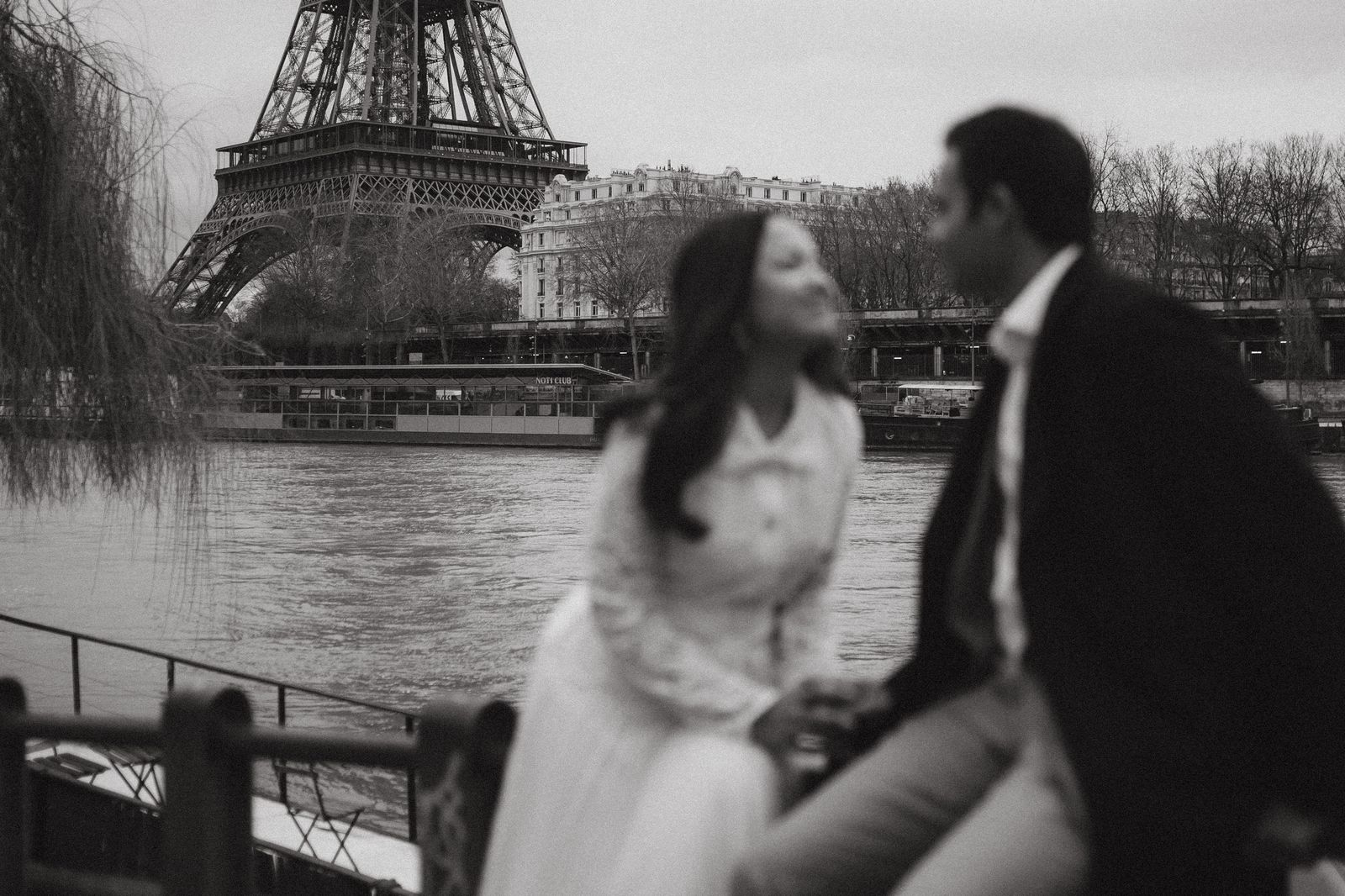 A couple in formal wedding attire posing near the water in a tropical city environment.