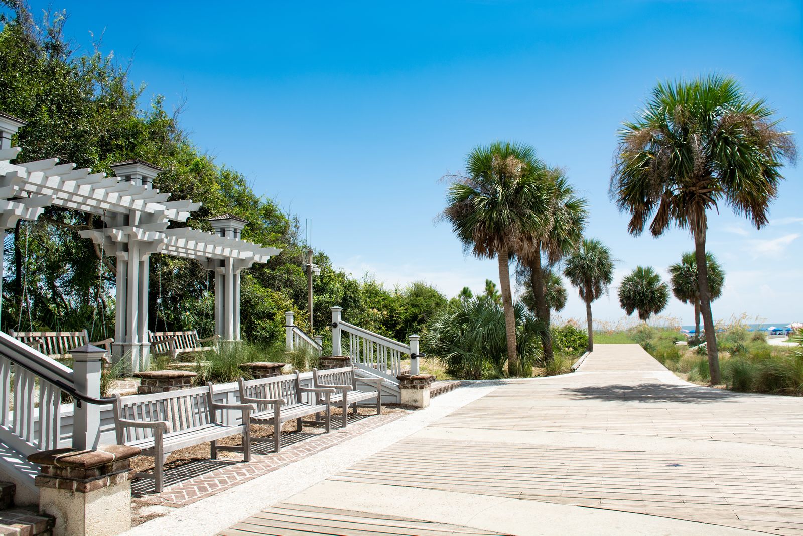 A peaceful park path with a wooden bench and green grass near the coast.