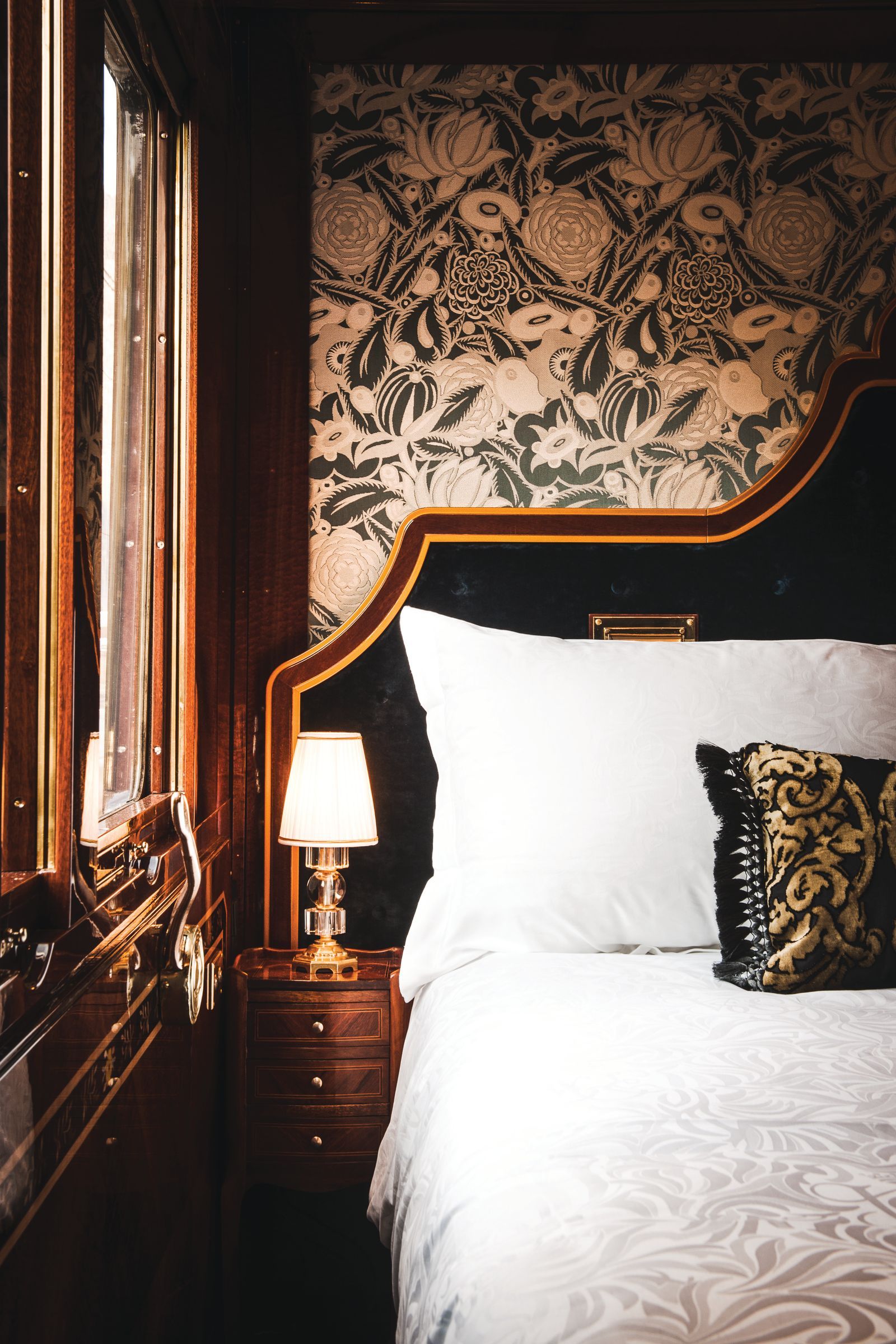 Interior of a luxury train sleeper cabin with a plush bed, warm lamp lighting, and high-end decor.