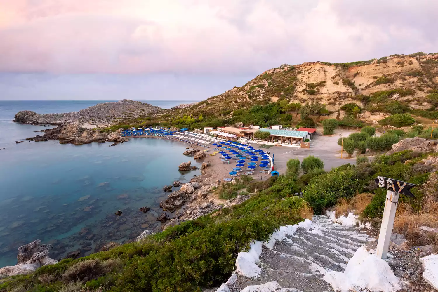 A view of the turquoise waters and rocky shoreline of Ladiko Beach near Anthony Quinn Bay.