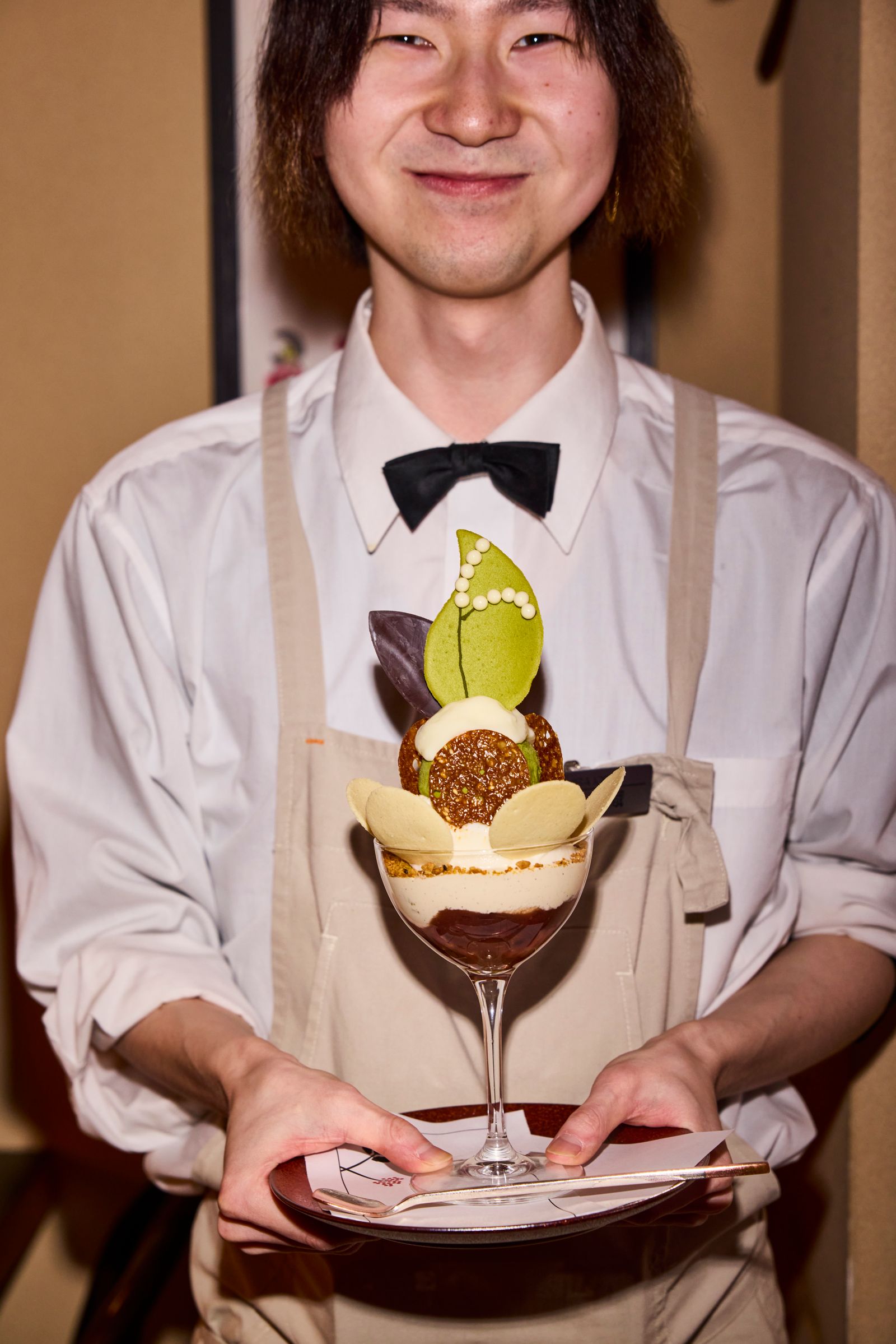 A person holding an elaborate, multi-layered Shime parfait in a Sapporo dessert shop.