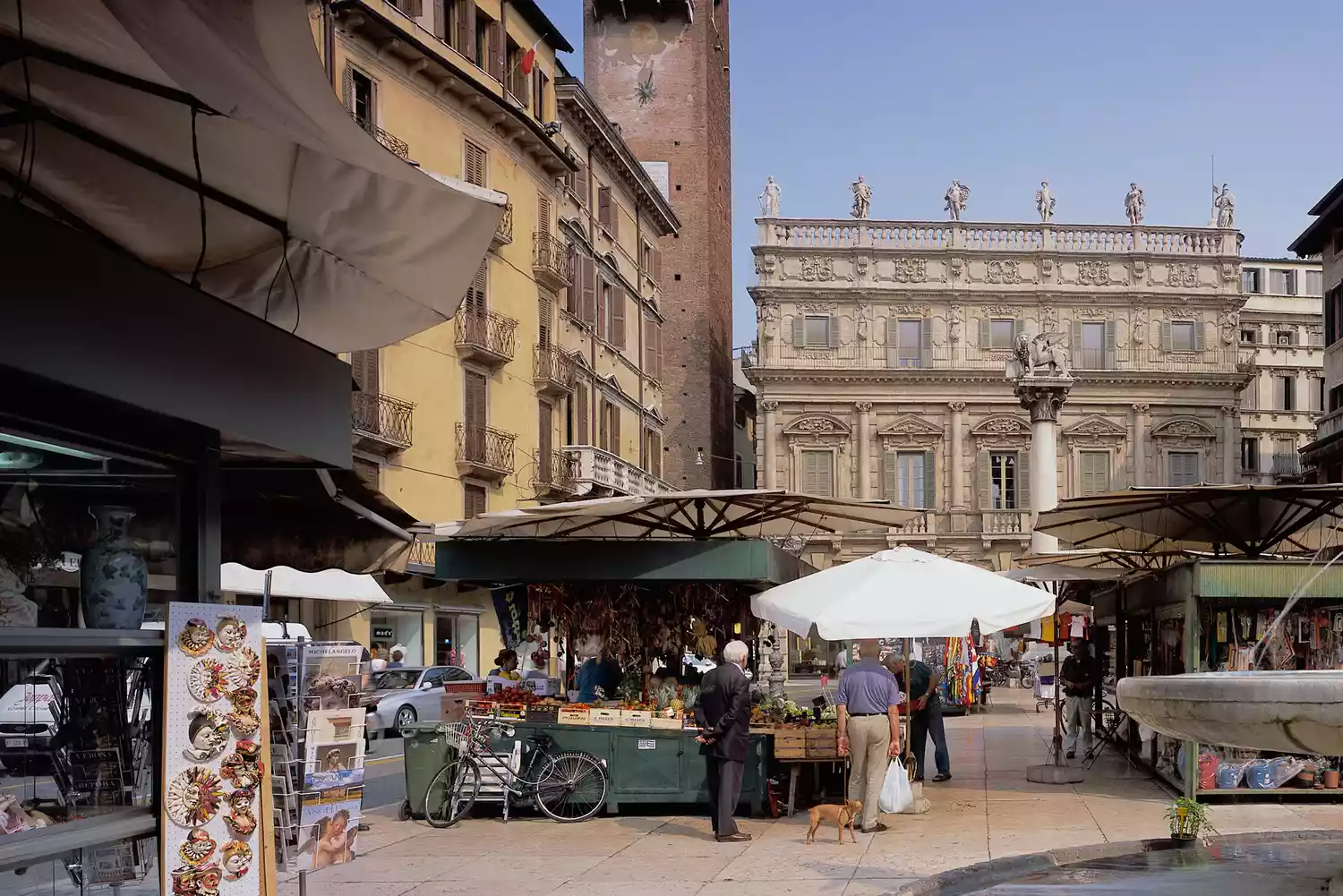 Outdoor market stalls under umbrellas in the historic Piazza delle Erbe.