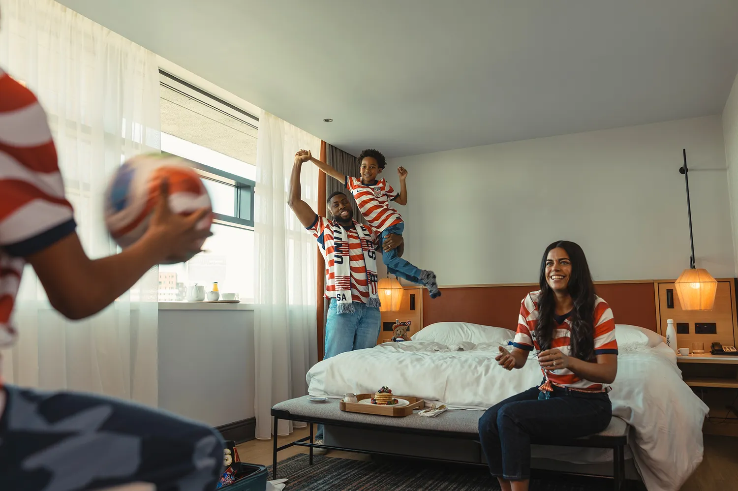 A family in a Marriott hotel room wearing USA soccer jerseys and holding a ball.