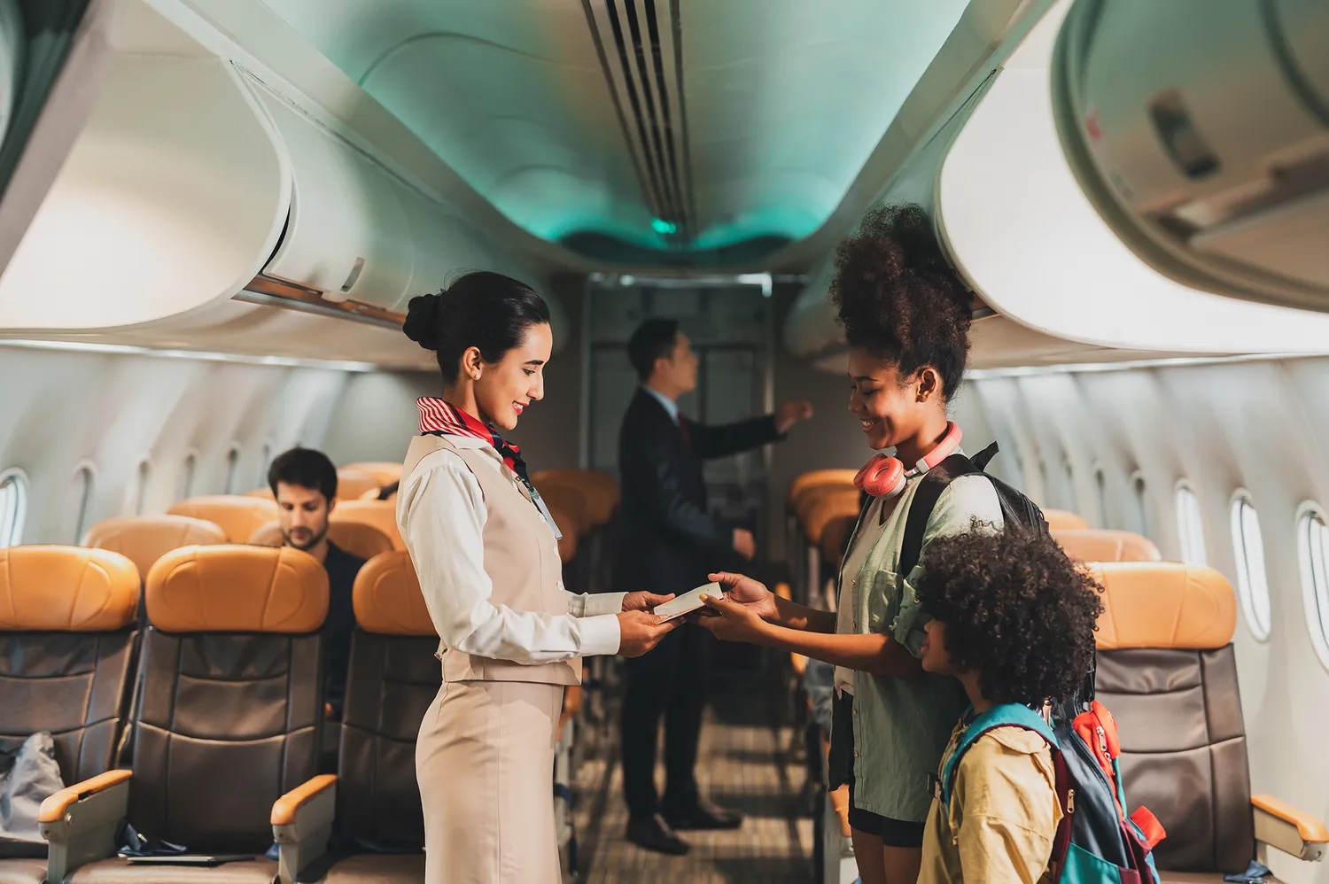A flight attendant in uniform assisting a passenger and a young child in the aisle of an airplane.