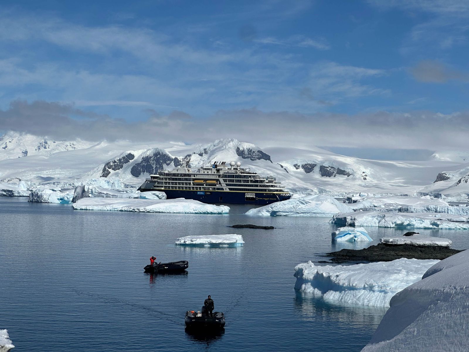 A large expedition vessel positioned among glacial ice and snow-capped mountains in Antarctica.