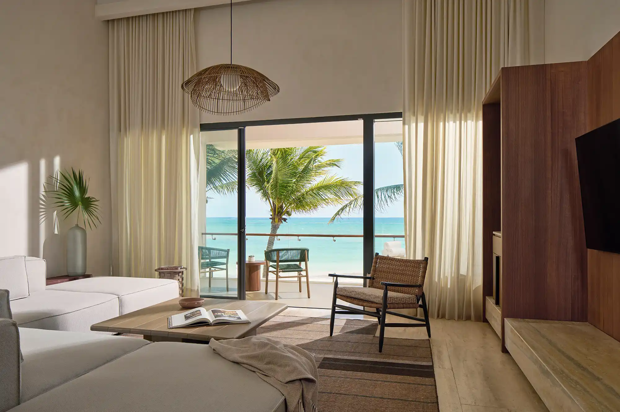 A sunlit living room with large windows facing a beach and ocean view.