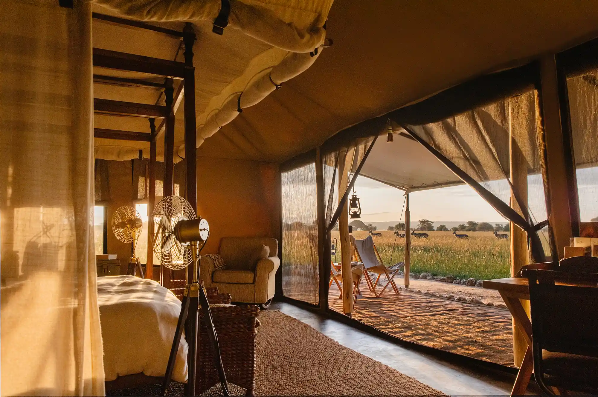 Interior of a luxury safari tent with high-end furnishings and a private deck overlooking the savannah.