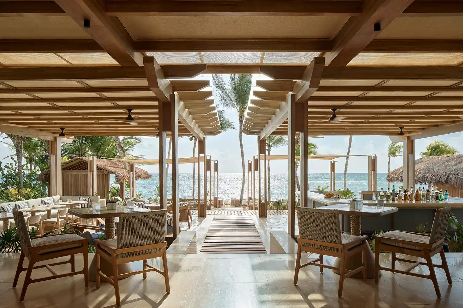 Open-air beachfront restaurant with wooden furniture and a view of the ocean.