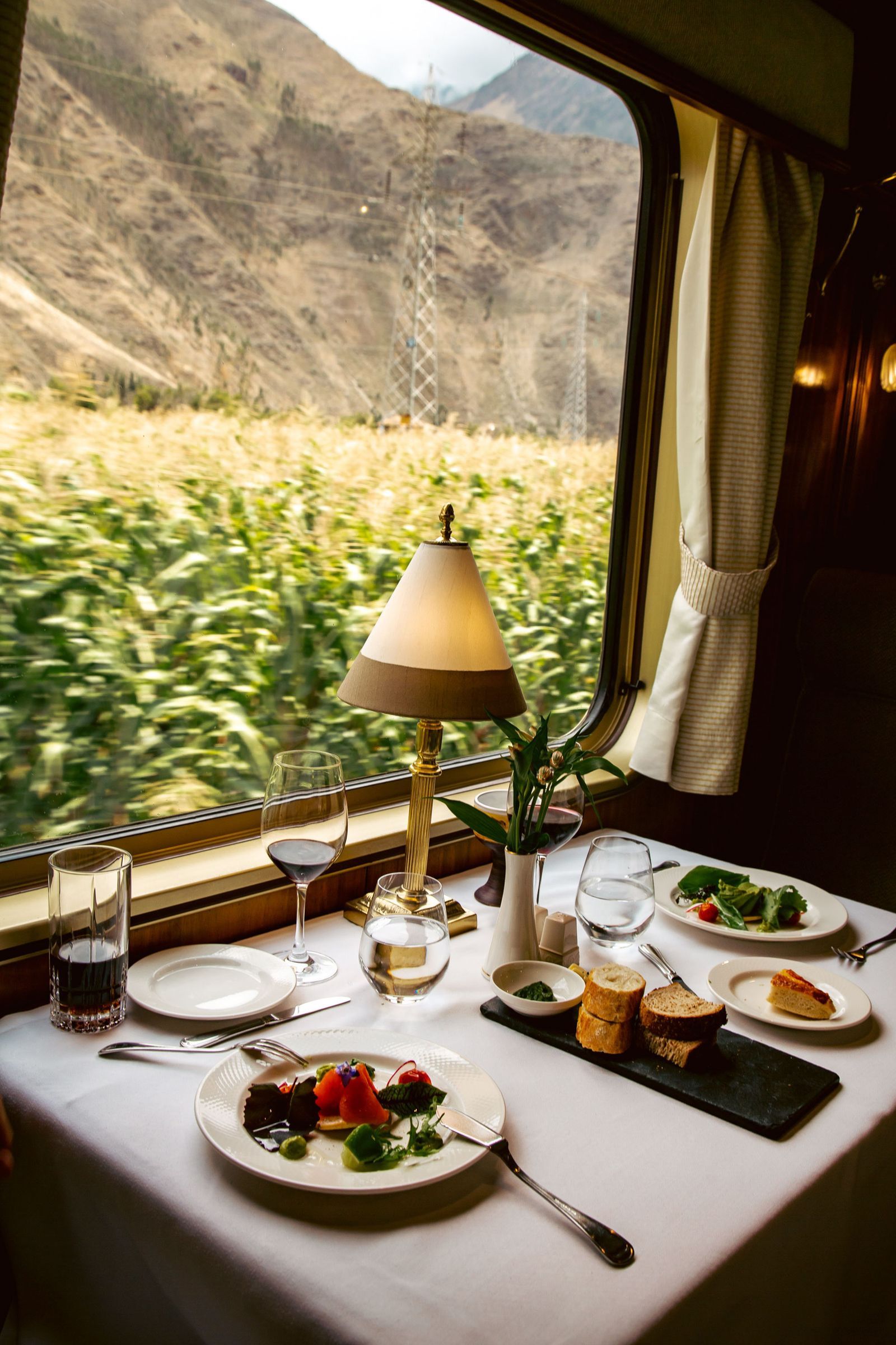 Table setting in a luxury train dining car featuring fine china, glassware, and elegant table lamps.