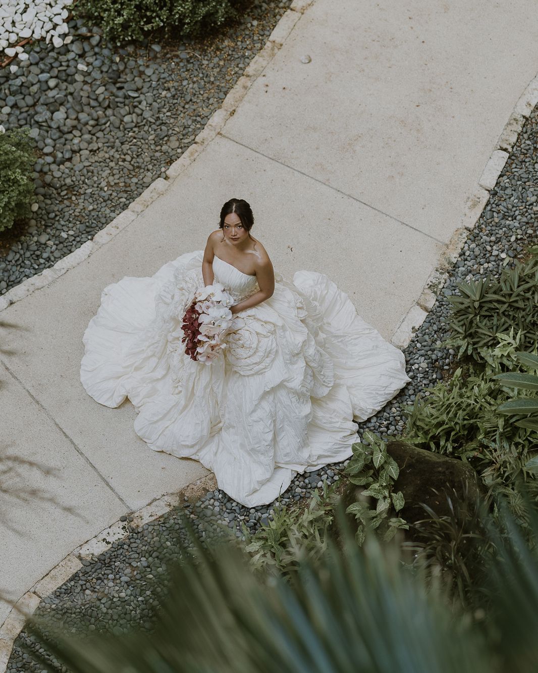 A bride in a white wedding gown walking along a manicured path at a luxury tropical resort.
