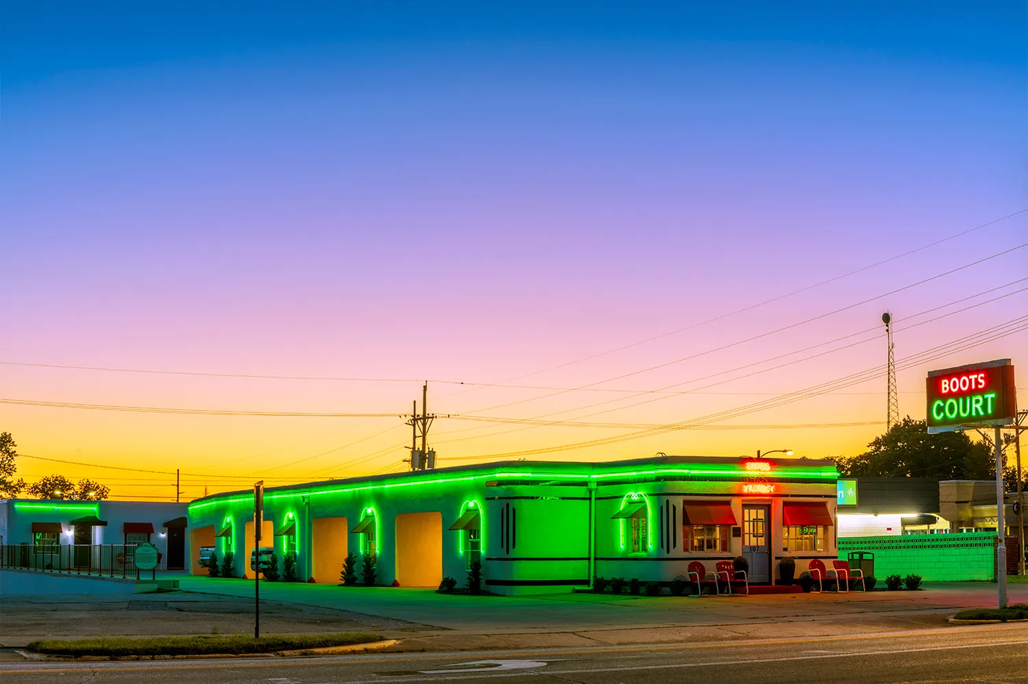 Retro exterior of Boots Court Motel in Carthage, Missouri, illuminated with neon green lights.