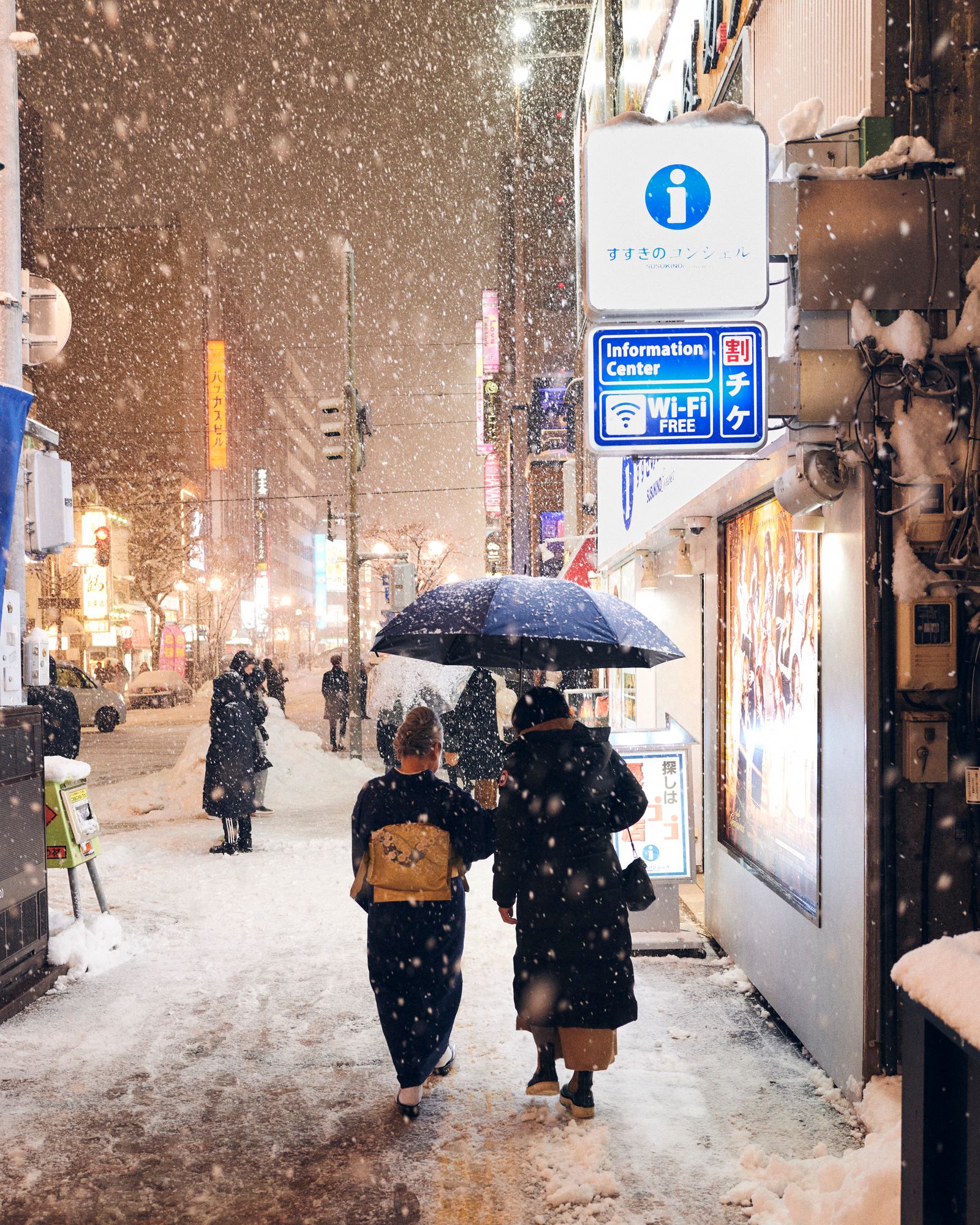 A person walking through a snowy Sapporo street with urban light trails in the background.