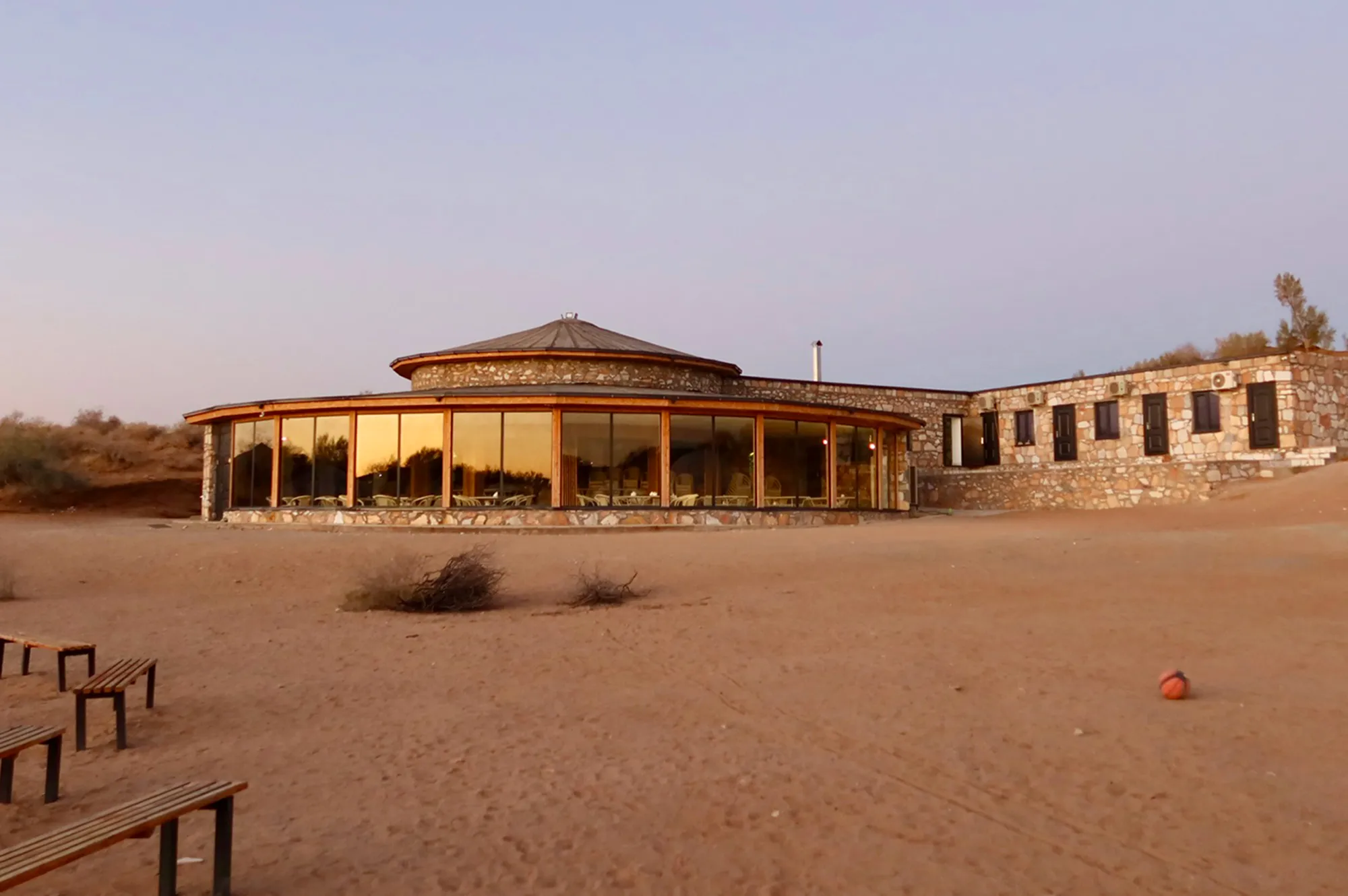A modern circular building with large windows used as a communal dining hall in the desert.