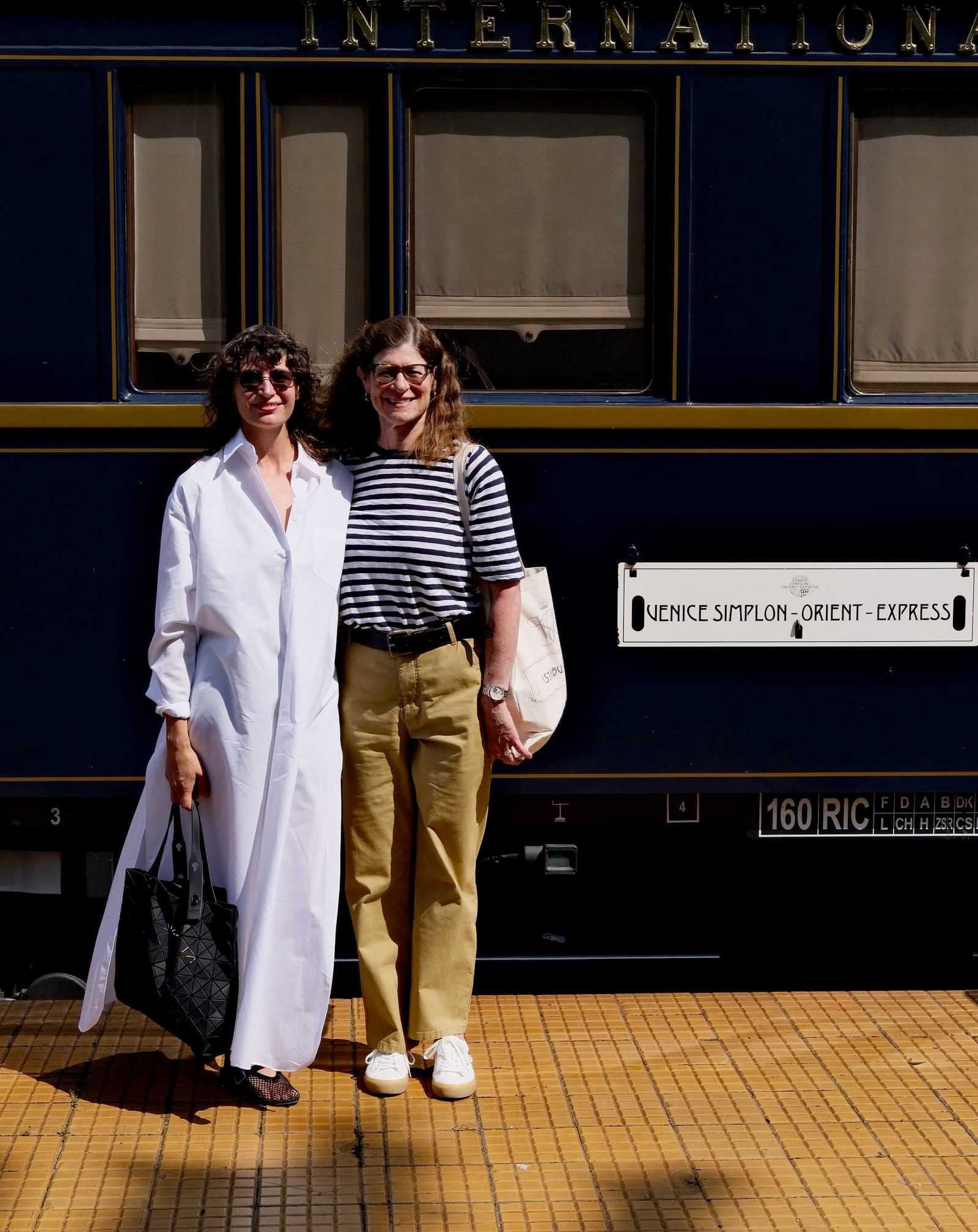 Two travelers in elegant clothing carrying luxury handbags, representing a mother-daughter duo.