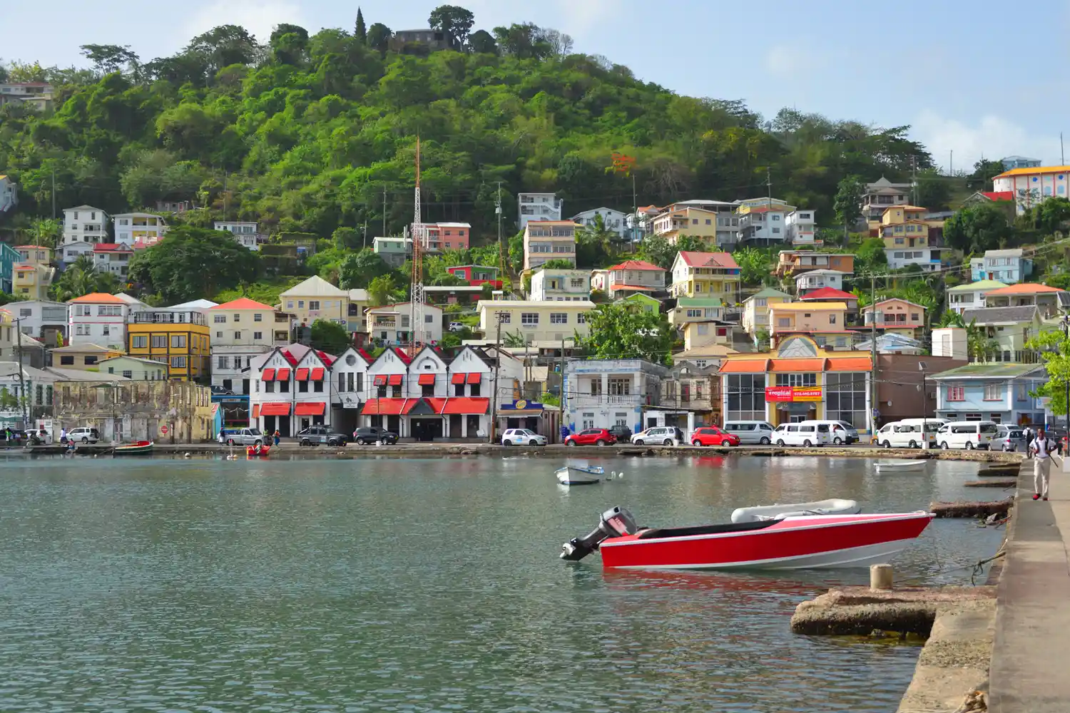 Colorful colonial-style buildings along the water in Grenada with a docked red boat.