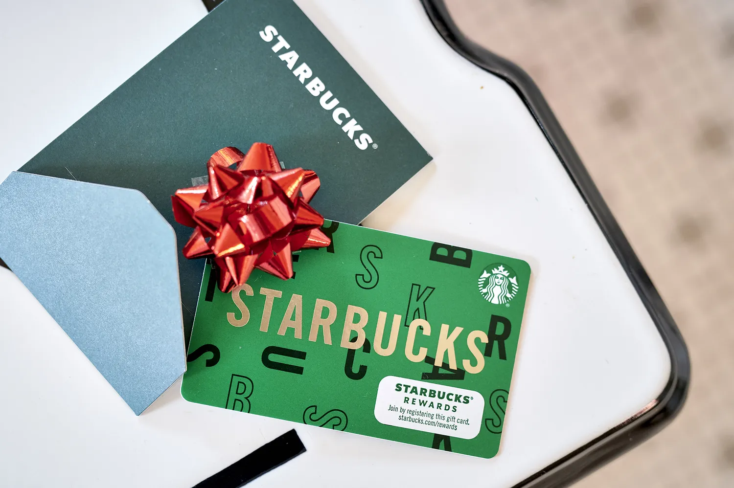 A Starbucks gift card with a red ribbon placed next to an envelope on a wooden surface.