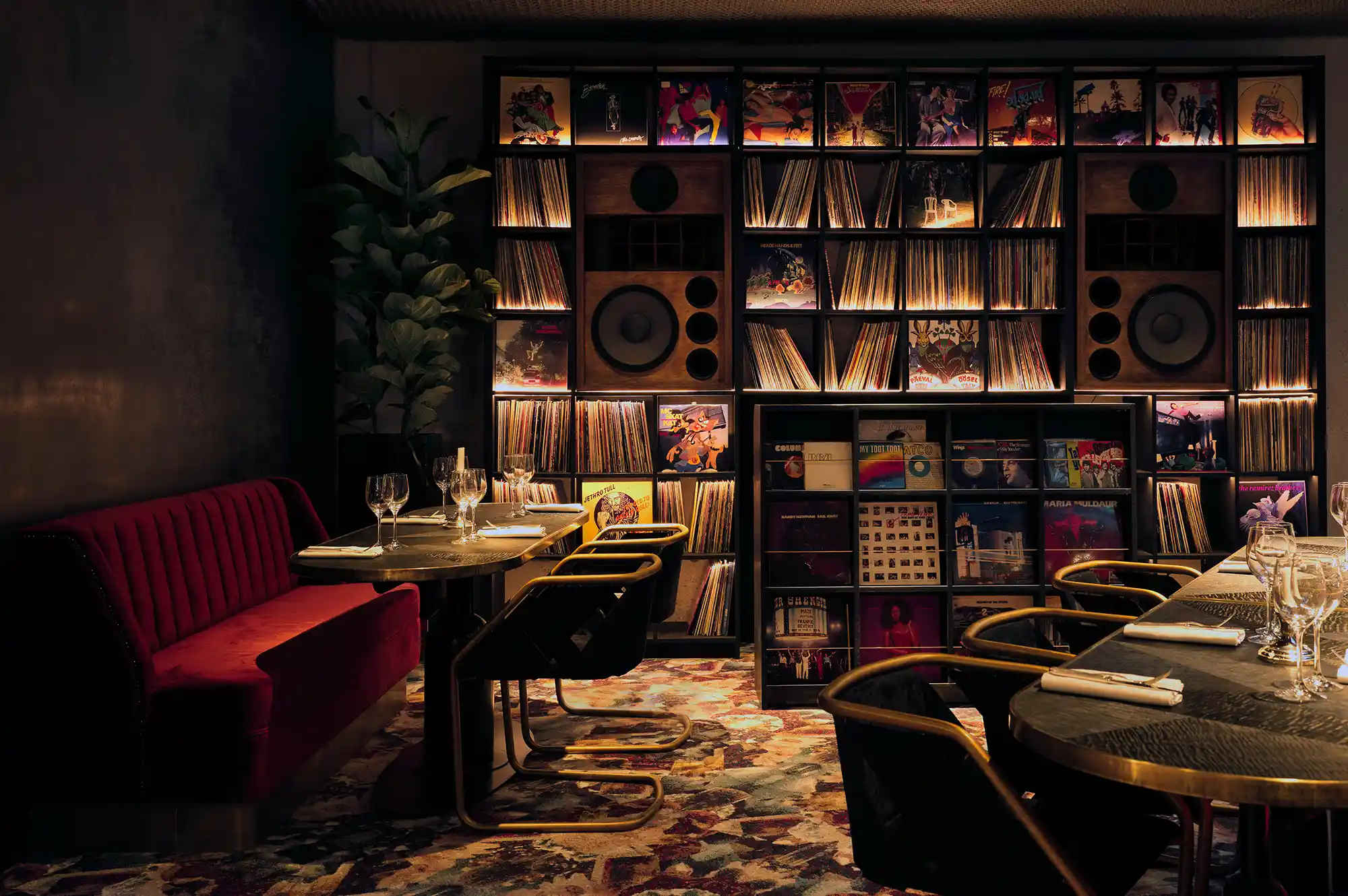 A dining area featuring a prominent back wall of vinyl records and large Ojas speakers.