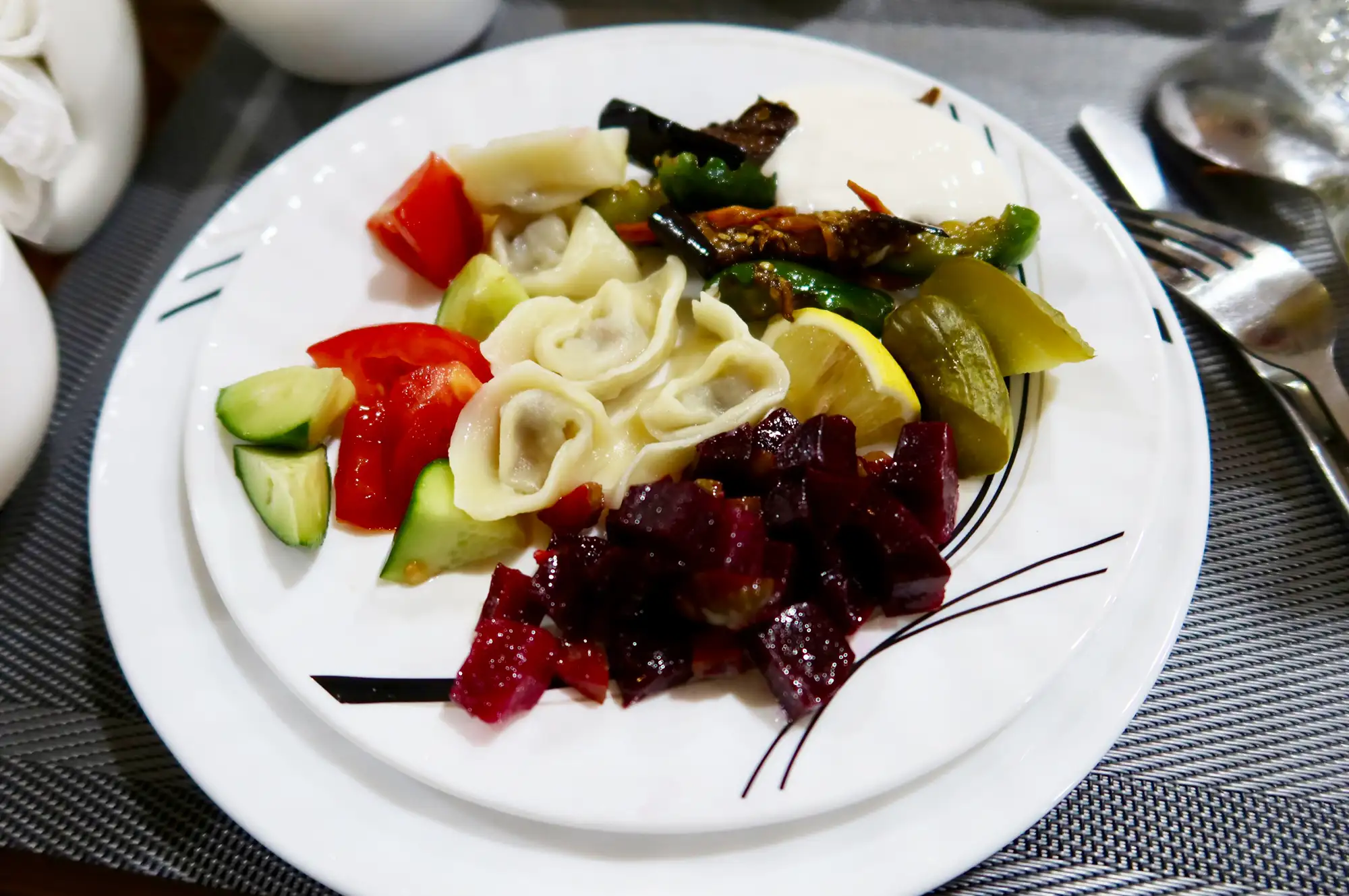 A plate of Uzbek dumplings with fresh vegetable garnishes on a traditional tablecloth.